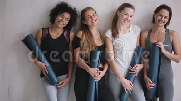 穿着运动服手持瑜伽垫摆在室内的漂亮多民族女孩视频的预览图