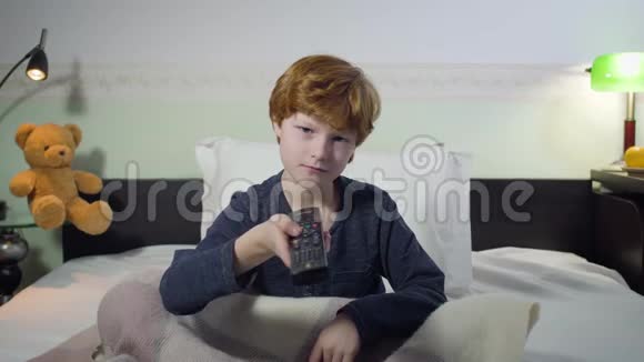 可爱的白种人小男孩的头像切换频道作出感兴趣的面部表情并看电视红头发视频的预览图