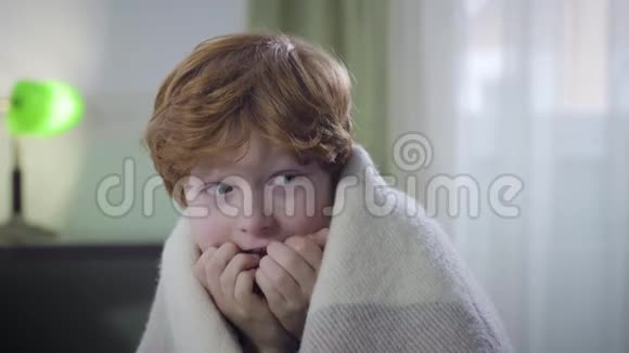 惊恐万状的白种人红头发男孩坐在室内被毯子覆盖环顾四周孩子离开了视频的预览图
