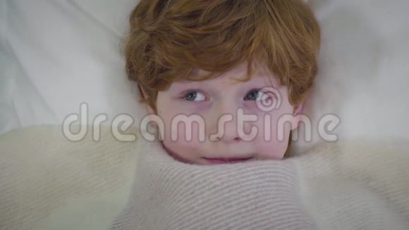 红发白种人男孩的特写灰色的眼睛躺在毯子下环顾四周一个人躺在床上的小孩视频的预览图
