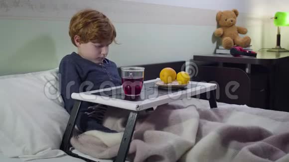 悲伤的白种人红头男孩躺在床上喝着热果茶病童卧床的肖像视频的预览图