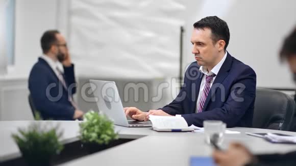 专注的商人西装享受工作坐在办公桌上的白色房间内部红色乌鸦相机视频的预览图