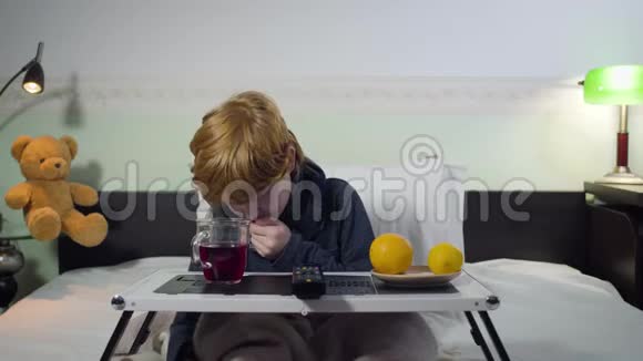 一幅白人小男孩带着遥控器和电视频道切换咳嗽的肖像红头发可爱的孩子坐着视频的预览图