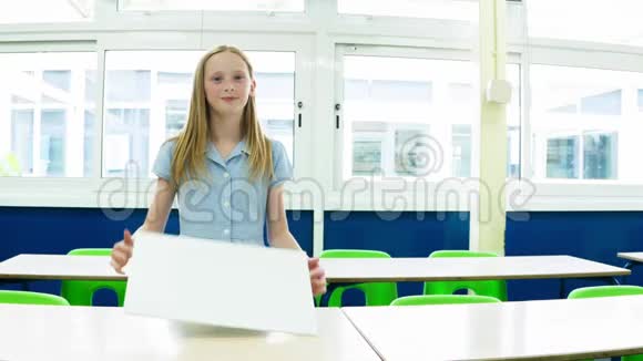 白人小学女孩在教室里举着一张空白的标语牌视频的预览图