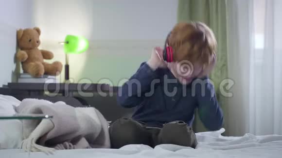 小白种人男孩在听耳机里的摇滚乐时会有感情地摇头可爱的红头发孩子坐在他的视频的预览图