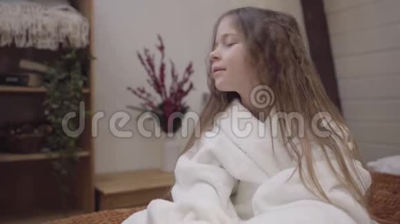 可爱的黑发小女孩摇动长发的特写肖像微笑快乐的孩子坐在床上看着镜头视频的预览图