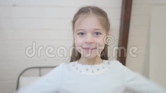 微笑的白种人女孩的特写肖像灰色的眼睛落在床上快乐的小女人在卧室里玩视频的预览图