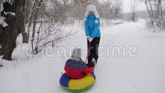 快乐的母亲骑着一个孩子在白色的雪道上雪橇上圣诞节假期成人和儿童的有趣游戏这就是视频的预览图