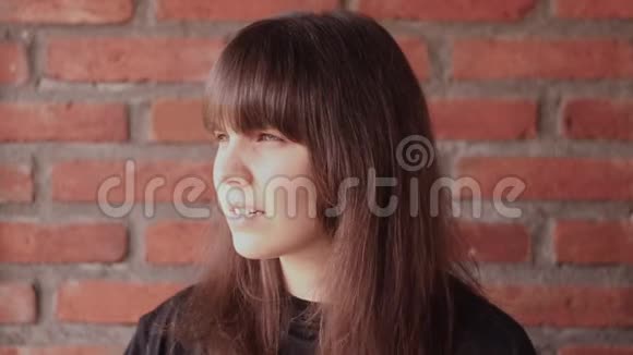 年轻的黑发女人穿着黑色t恤刘海翻了一番令人惊喜并在砖墙背景下欢欣鼓舞视频的预览图