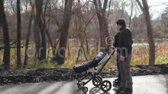 幸福的年轻家庭在公园里溜冰爸爸妈妈正在和婴儿车里的一个婴儿轮滑安全视频的预览图