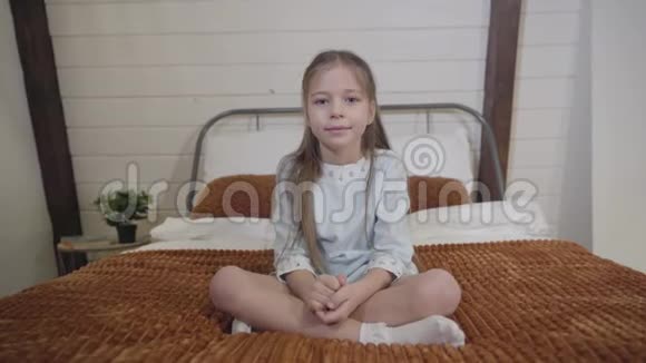 镜头接近可爱的黑发白种人女孩灰色的眼睛坐在床上看着相机微笑的孩子视频的预览图