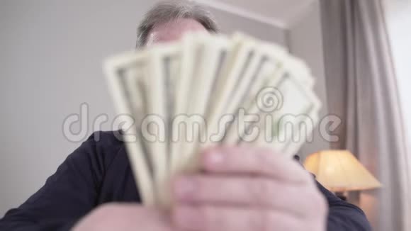 现金迷放成束高加索人戴着眼镜微笑持有美元钞票的富裕退休人员画像视频的预览图