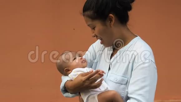 幸福的亚洲母亲抱着他刚出生的可爱婴儿穿衣服的肖像妈妈用爱和关怀拥抱她的孩子她视频的预览图
