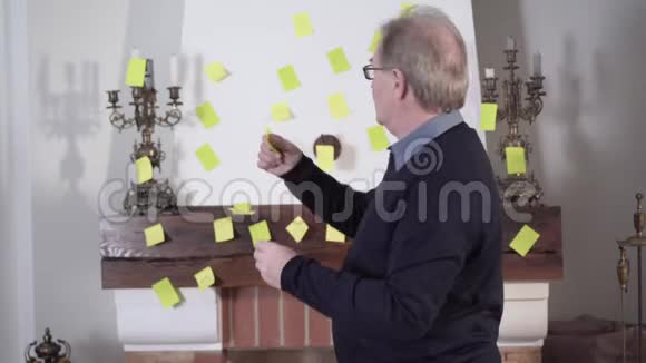 一个白人老人把笔记贴在墙上把拇指对着镜头正面老退休人员肖像视频的预览图