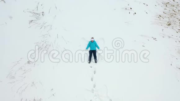 一个女孩在森林的空地上做一个雪天使的身影一个女孩躺在雪地里的空中摄影视频的预览图