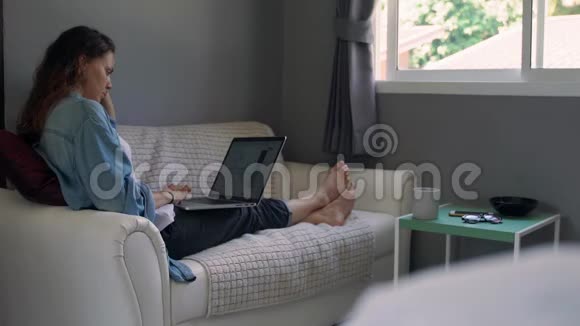 一位年轻女子手提电脑坐在客厅的沙发上视频的预览图