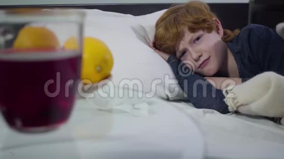 病态的白人小男孩躺在床上对着镜头转过身来热饮和橙子视频的预览图