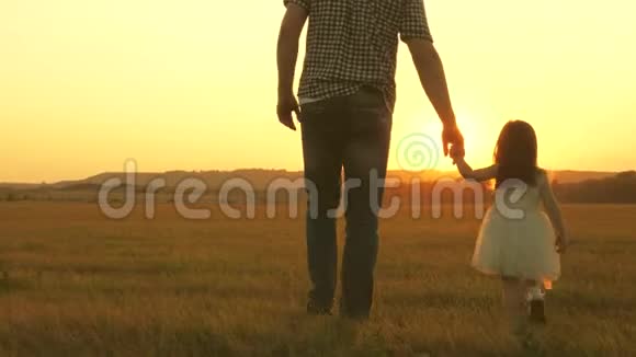 小女儿和她父亲牵着手在草地上散步孩子握着父亲手一家人晚上出去散步视频的预览图