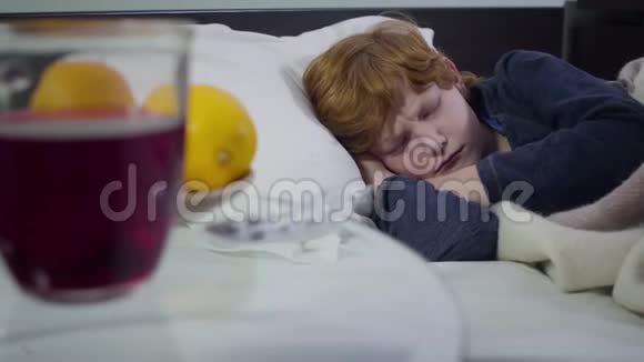 恶心的白人可爱男孩躺在床上吃药的特写镜头可怜的红头发孩子呆在家里的画像视频的预览图