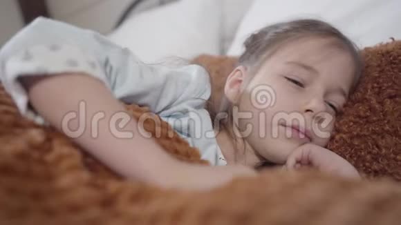早上伸展身体的漂亮白种人女孩的特写照片可爱的黑发孩子躺在床上休闲休闲视频的预览图