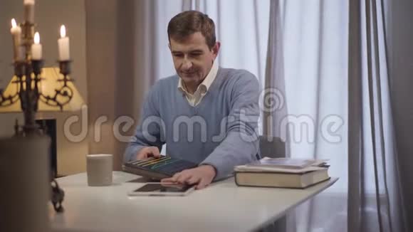 镜头接近面对一个快乐的白人中年男子坐在桌旁桌上放着平板电脑和相册视频的预览图