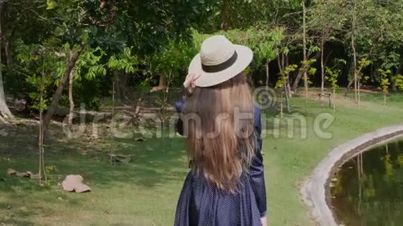 夏日热带公园漫步湖畔的草帽女游客视频的预览图