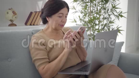 成熟的高加索女人轻敲智能手机屏幕并微笑积极的高级女商人上网视频的预览图