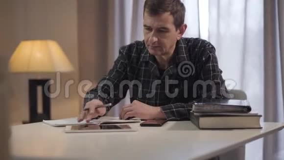 成年男性白种人自由职业者在家工作的肖像中年人用平板电脑写笔记视频的预览图