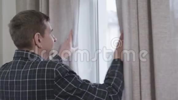 中年白种人的肖像戴着耳环打开窗帘早上看着窗外成年男子视频的预览图