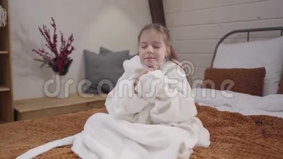 镜头接近迷人的白种人女孩美丽的眼睛坐在床上穿着白色的浴袍肖像视频的预览图
