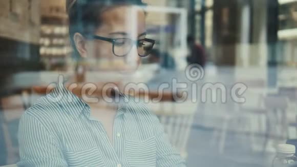 一个戴眼镜的女人从咖啡馆的窗户里拍下来视频的预览图