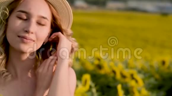 戴着帽子站在向日葵的田野上美丽欢快的女孩的特写肖像视频的预览图