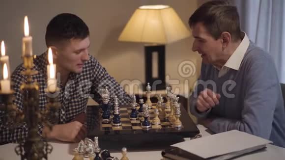 一幅聪明的中年白种人教他成年儿子下棋的画像两个人在家过夜视频的预览图