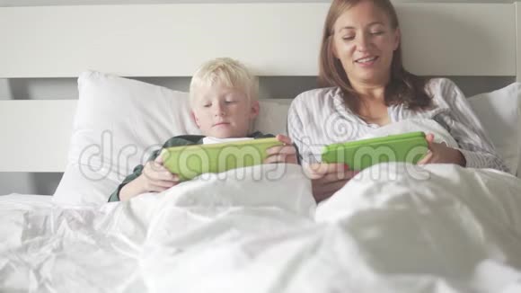 妈妈和儿子早上躺在床上检查平板电脑上的社交网络视频的预览图