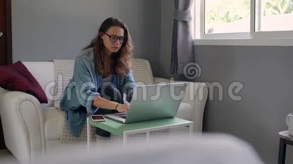 一位年轻女子手提电脑坐在沙发上举行在线咨询视频的预览图
