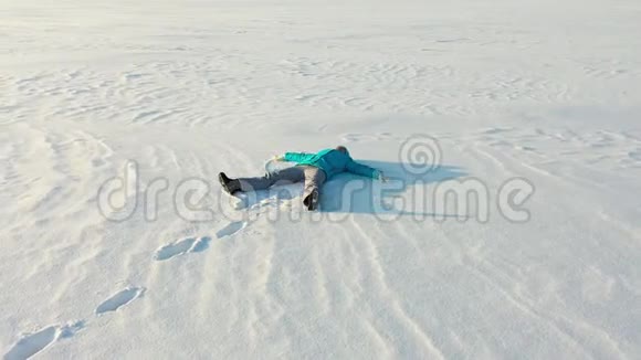 一个女孩在森林的空地上做一个雪天使的身影一个女孩躺在雪地里的空中摄影视频的预览图