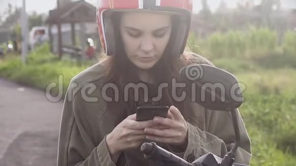 女孩旅行者在电话里发短信在日出时停在路边的自行车上视频的预览图