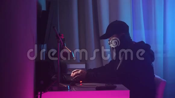 男性黑客坐在办公桌旁闯入系统黑色连帽衫黑色头巾遮住脸视频的预览图