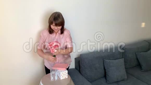 女人把一束粉红色的康乃馨放在花瓶里微笑着盒子里的礼物放在圆桌上节日的概念情人节视频的预览图