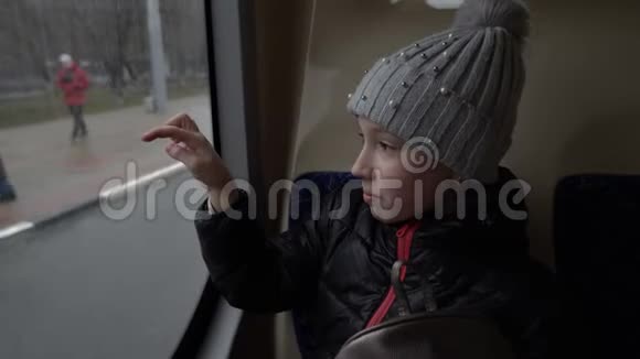 一个戴着帽子的可爱小女孩坐在公共汽车后座的玻璃上画画从窗口经过的人视频的预览图