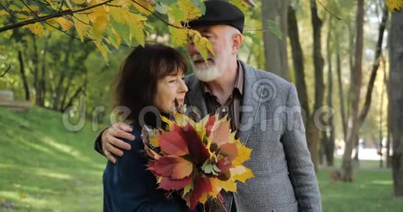 在一个舒适的秋城公园里一对幸福的老夫妇在温暖的天气里微笑着拥抱有叶子的老太太视频的预览图