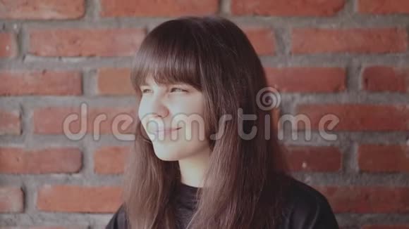 在砖墙背景上一位身穿黑色T恤衫头戴刘海的美丽黑发女子的肖像她快乐而微笑视频的预览图