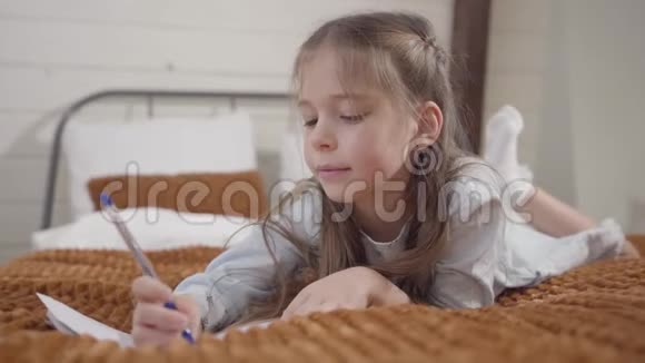 迷人的白人女孩躺在床上写字的肖像聪明的孩子展示了我的创意视频的预览图