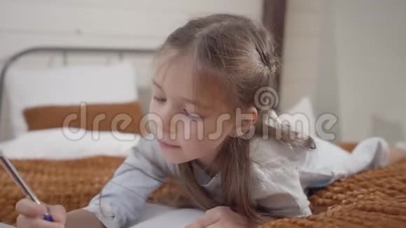 镜头接近可爱的小白种人女孩躺在床上和写作可爱开朗的孩子视频的预览图