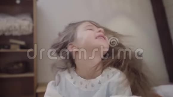 可爱的黑发小女孩摇动长发的特写肖像微笑快乐的孩子坐在床上看着镜头视频的预览图