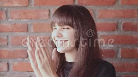 在砖墙背景上一位身穿黑色T恤衫头戴刘海的美丽黑发女子的肖像她快乐而微笑视频的预览图