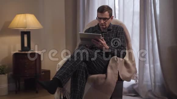 体贴的白种人中年男子摘下眼镜望着远处成年聪明人在室内使用平板电脑视频的预览图