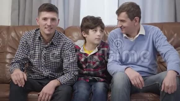 镜头接近小白种人男孩坐在沙发上拥抱他的父亲和祖父快乐男孩视频的预览图