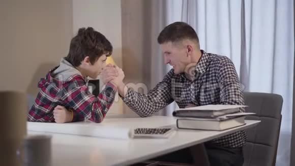 镜头接近快乐的白种人小男孩在与年轻父亲的手臂摔跤快乐的孩子赢了视频的预览图