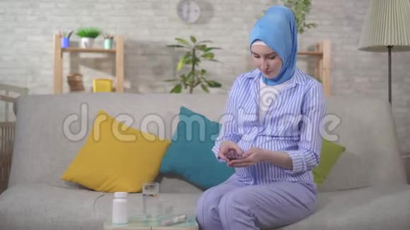 坐在沙发上吃药丸的年轻穆斯林孕妇视频的预览图